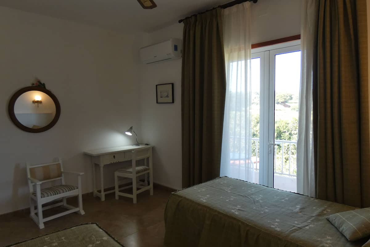 Een slaapkamer met een bed, een bureau, een stoel, een raam met gordijnen en een spiegel aan de muur.