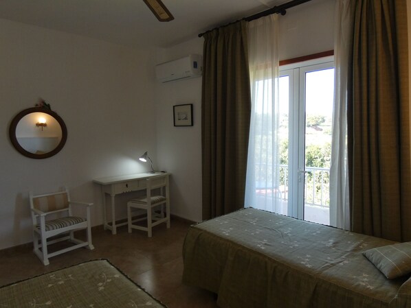 Un dormitorio con cama, escritorio, silla, ventana con cortinas y espejo en la pared.