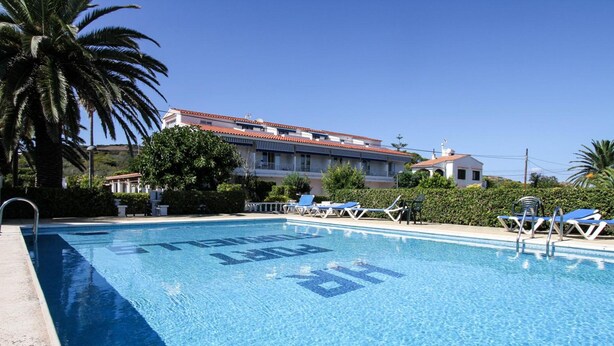 A swimming pool with lounge chairs and a building in the background. - Hostal Port Fornells - Adults Only (Mercadal)