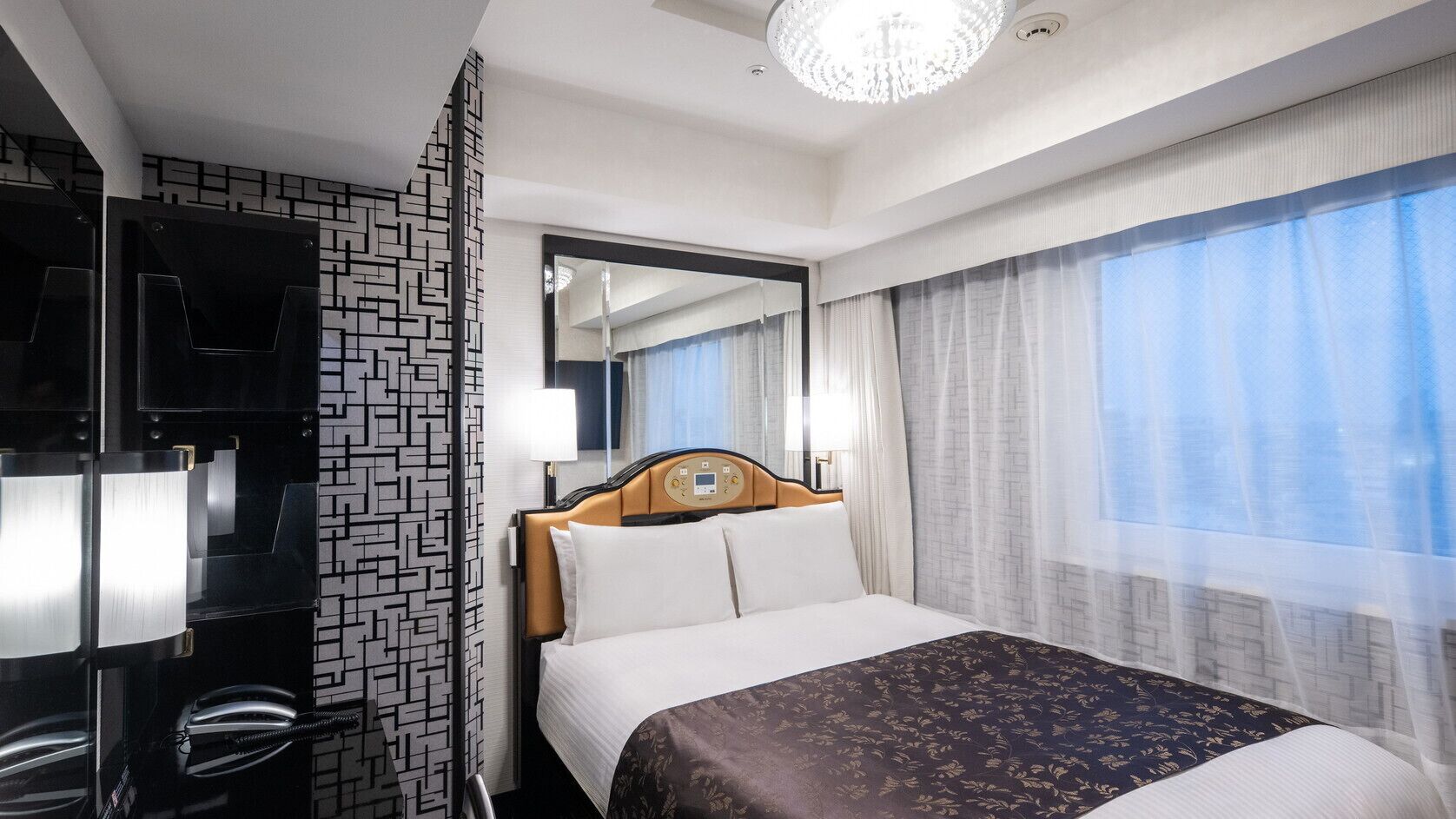 A hotel room with a bed, a TV, a mirror, and a window with curtains.