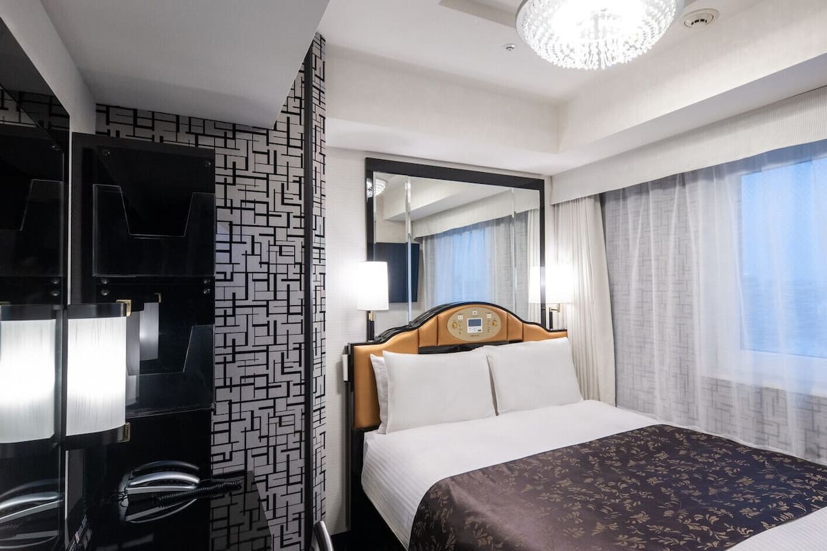 Une chambre d’hôtel avec un lit, une télévision, un miroir et une fenêtre avec des rideaux.