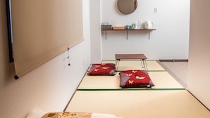 A traditional Japanese-style room with tatami flooring, a low bed with white bedding, a hanging shoji screen, a wooden ceiling, and a small shelf with toiletries. - Kujira 301 (Osaka)