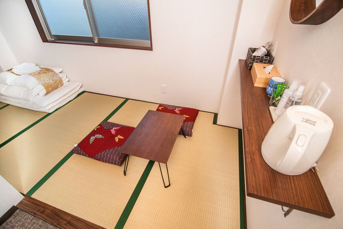 A tatami mat room with a wooden table, a sofa, and a small shelf with toiletries.