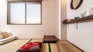 A room with tatami flooring, a sliding door window, a small table, a shelf with toiletries, and a mirror on the wall. - Kujira 301 (Osaka)