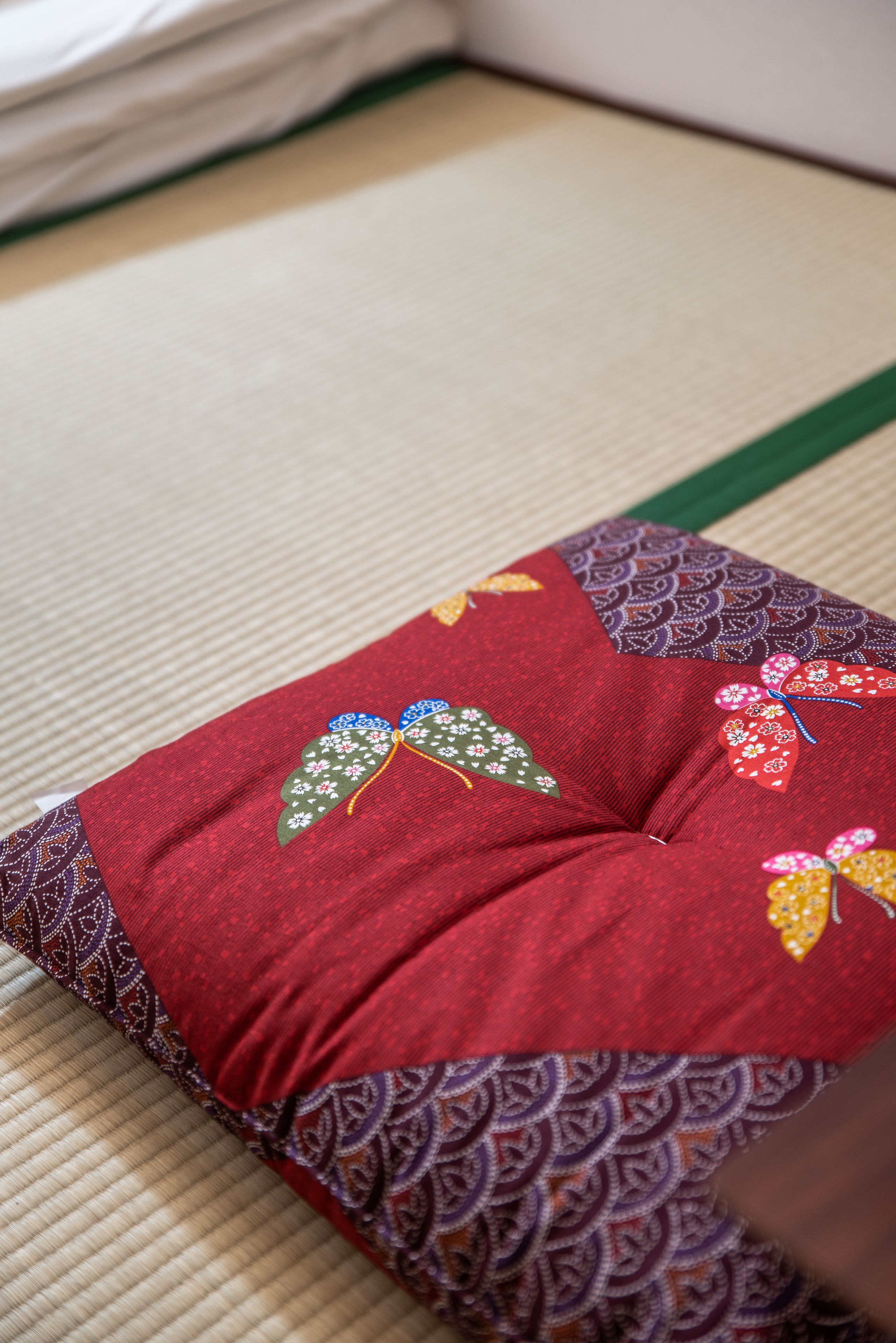 Ein rotes Kissen mit Blumenstickerei auf einer Tatami-Matte.