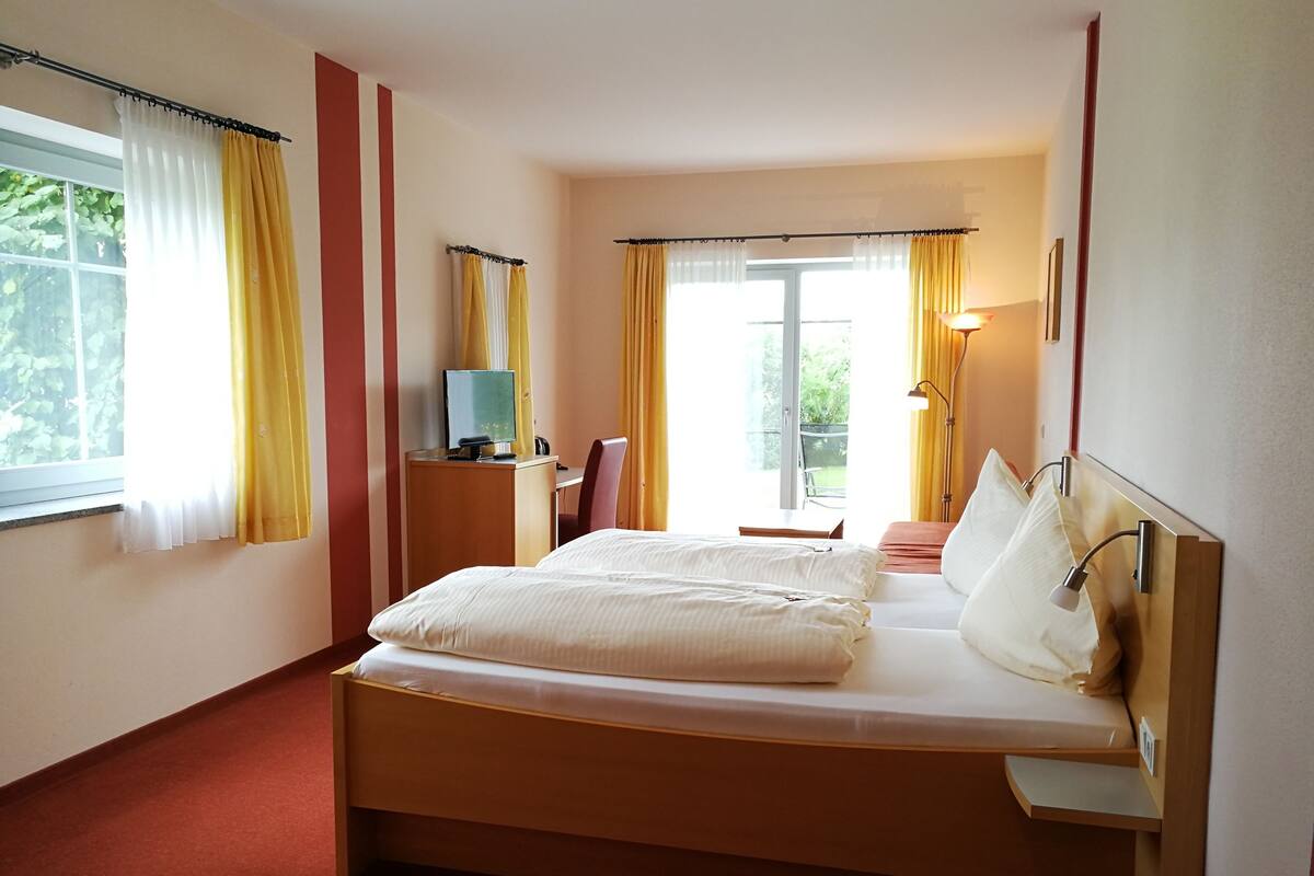 A hotel room with a bed, a desk with a computer, a chair, and a window with curtains.