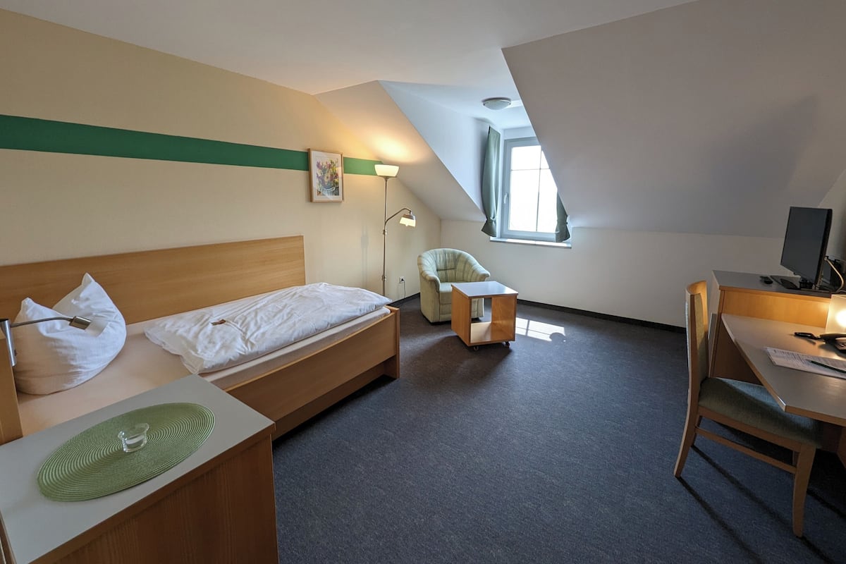 A hotel room with a bed, a desk, a chair, a lamp, and a window.