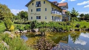 A two-story building with balconies, a pond with lily pads, and lush greenery. - Landhotel Larenzen (Kirchham)