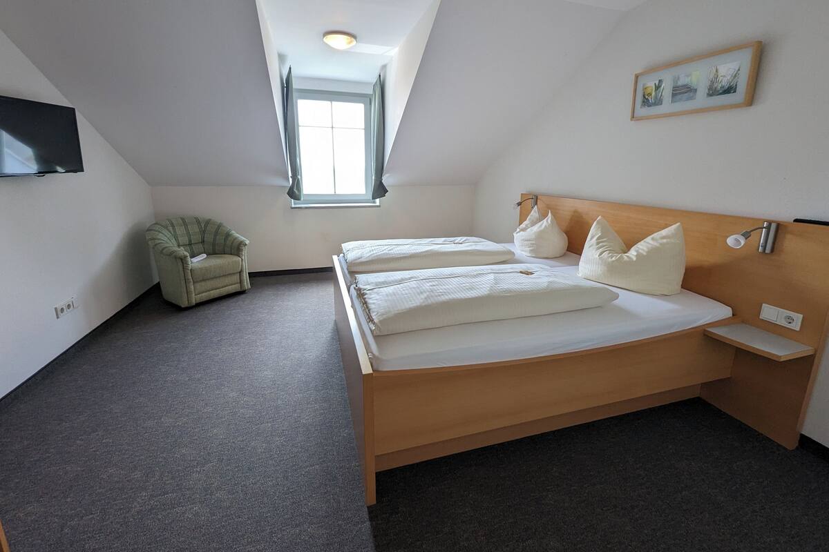 A hotel room with a large bed, a chair, a TV, a window, and a ceiling light.