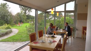 A dining area with two tables, chairs, and a view of a garden. - Landhotel Larenzen (Kirchham)