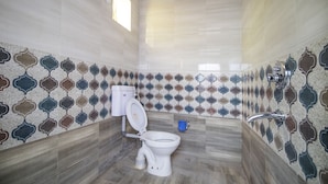 A bathroom with a toilet, a blue bucket, and patterned tiles on the walls. - Hotel Rudra (Majhgawan)