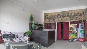 A reception area with a sofa, a glass table, a plant, a decorative wall, a Coca-Cola refrigerator, and a red curtain. - Hotel Rudra (Majhgawan)