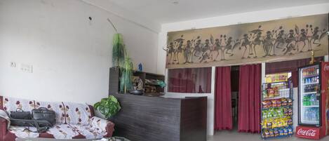 A reception area with a sofa, a glass table, a plant, a decorative wall, a Coca-Cola refrigerator, and a red curtain.