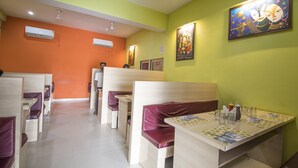 A restaurant with booths and tables, air conditioning units, and artwork on the walls. - Hotel Rudra (Majhgawan)