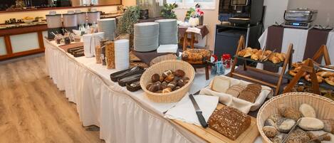 A breakfast buffet with various breads, pastries, and condiments.