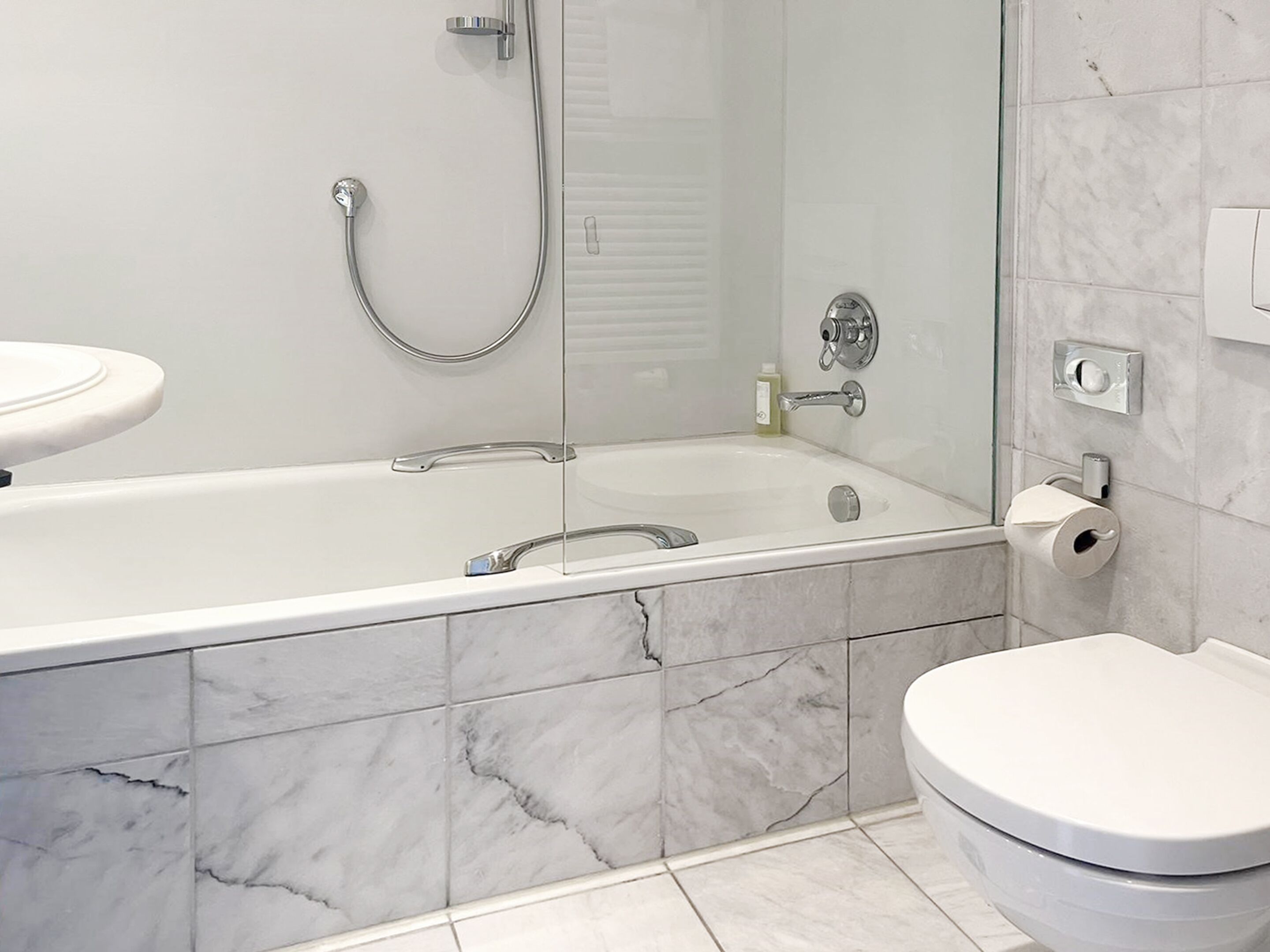 A modern bathroom with a glass-enclosed shower, a white bathtub, and a toilet.