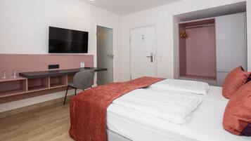Ein Hotelzimmer mit Bett, Schreibtisch, Stuhl, Fernseher und Kleiderschrank.