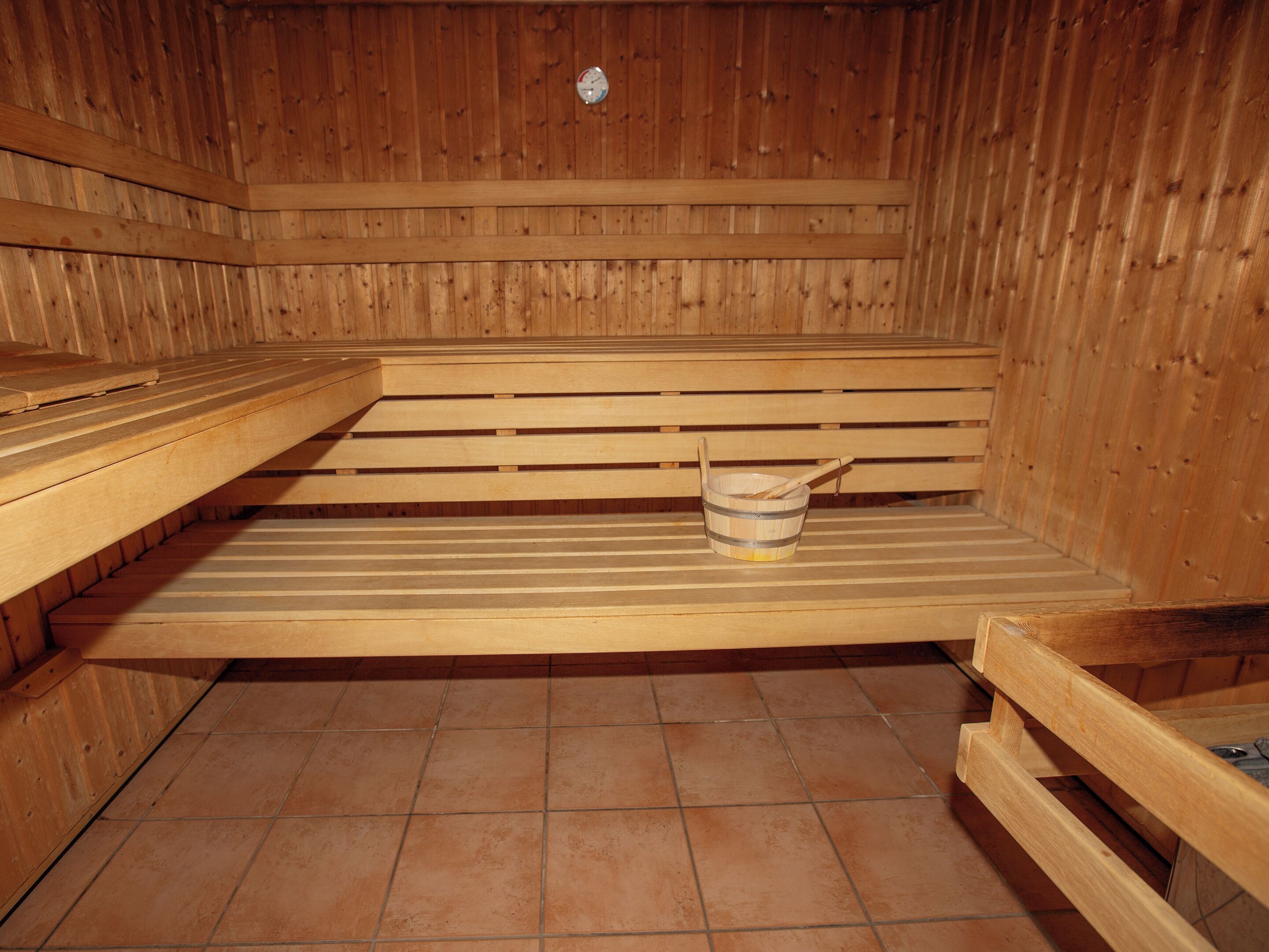 A sauna with wooden benches and a bucket with a wooden scoop.