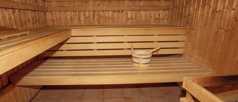 A sauna with wooden benches and a bucket with a wooden scoop.