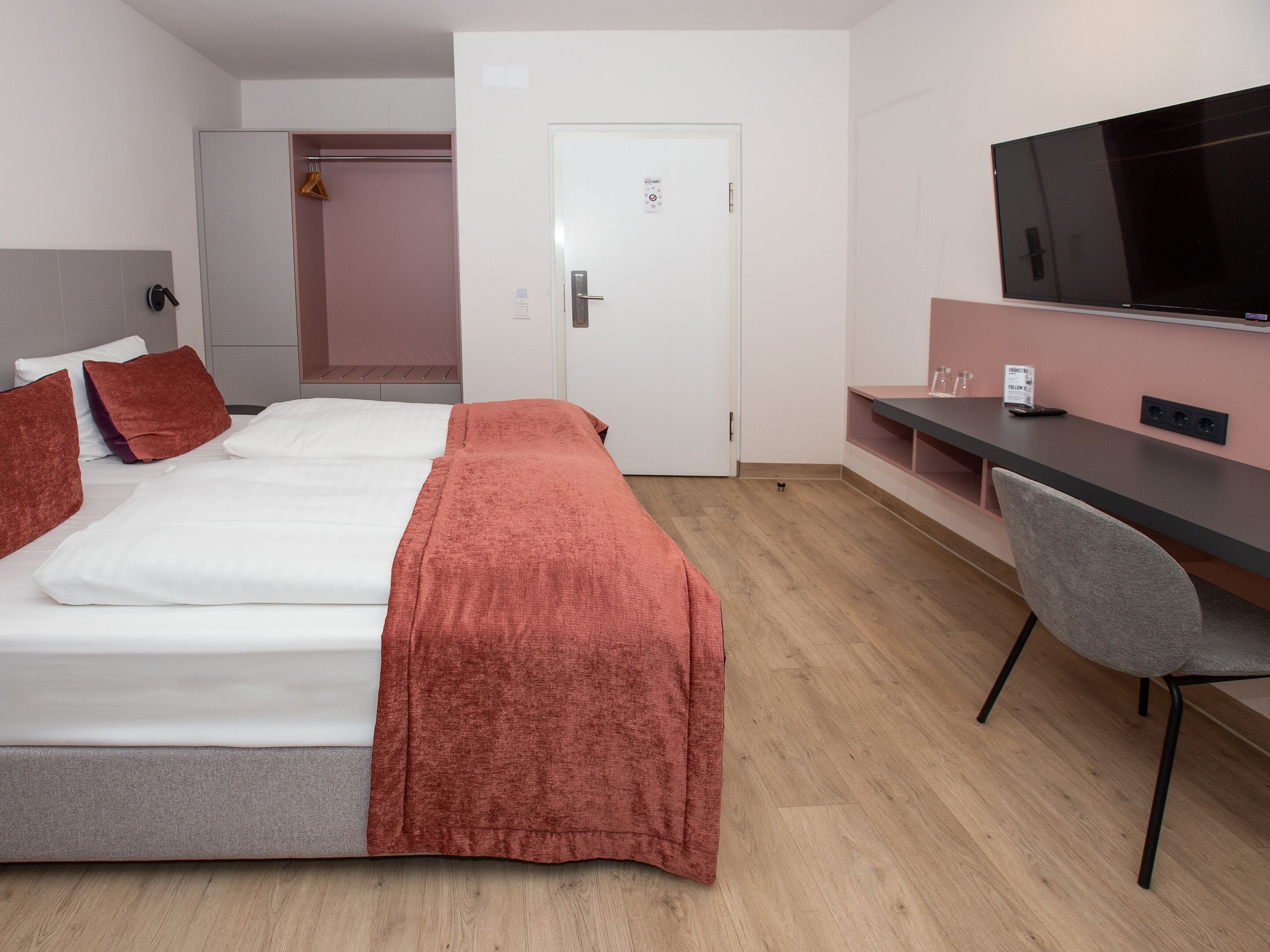 Hotellihuone, jossa on sänky, työpöytä, tuoli, televisio ja ovi.