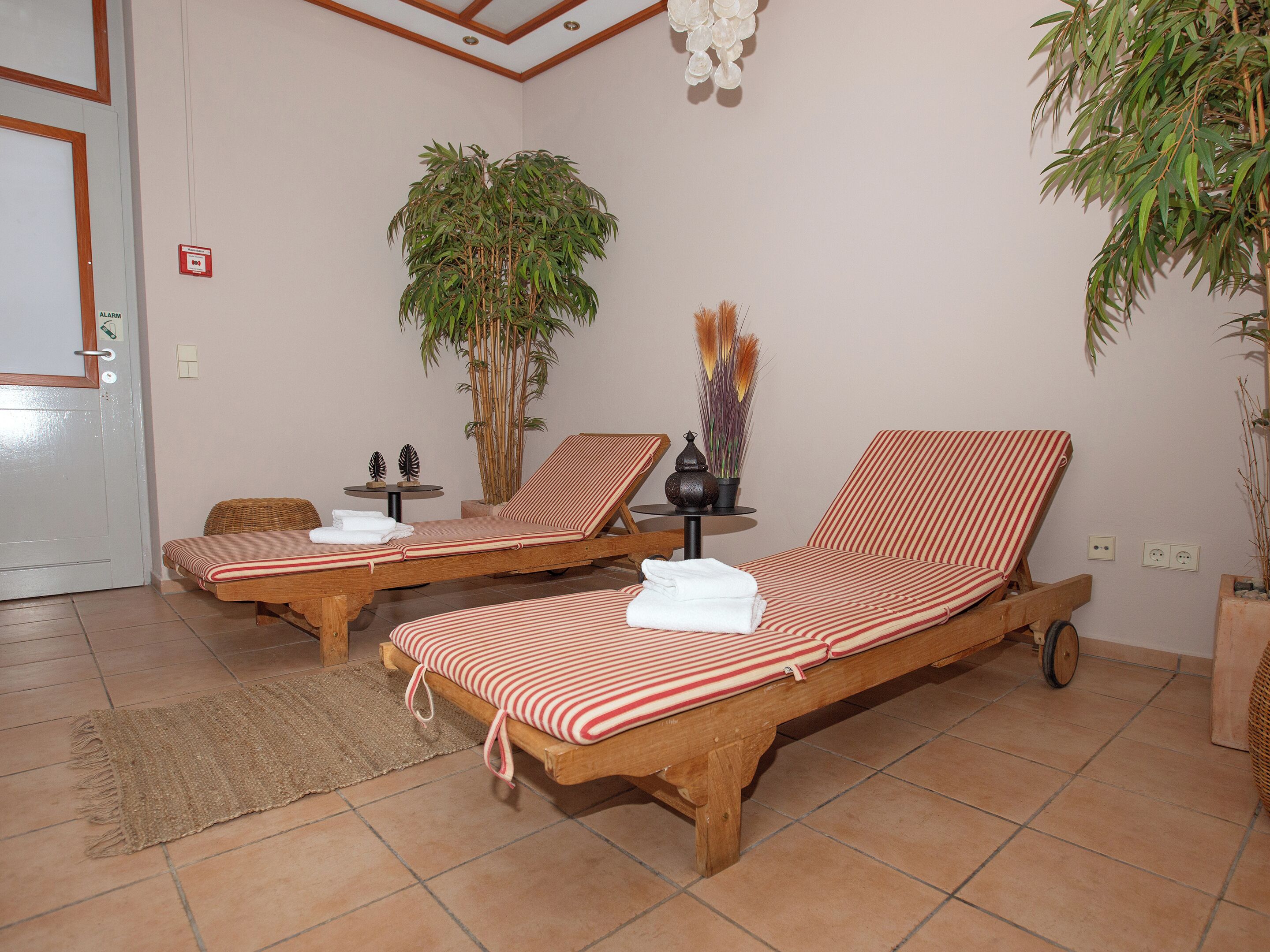 Una habitación con dos sillones de madera, una mesita con una planta y una puerta con un cartel de alarma.