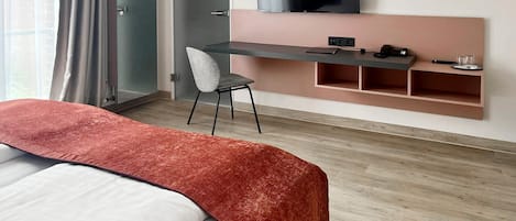 A hotel room with a bed, a desk, a chair, a TV, and a window with curtains.