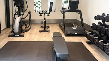 Un gimnasio con equipo cardiovascular, mancuernas y una banca.