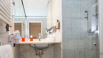 Ein modernes Badezimmer mit Duschkabine aus Glas, einem weißen Waschbecken mit Marmorplatte und einem großen Spiegel darüber.