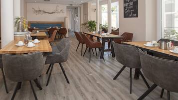 Una cafetería moderna con mesas de madera y sillas grises, que presenta un arte decorativo en la pared y una cita motivacional.