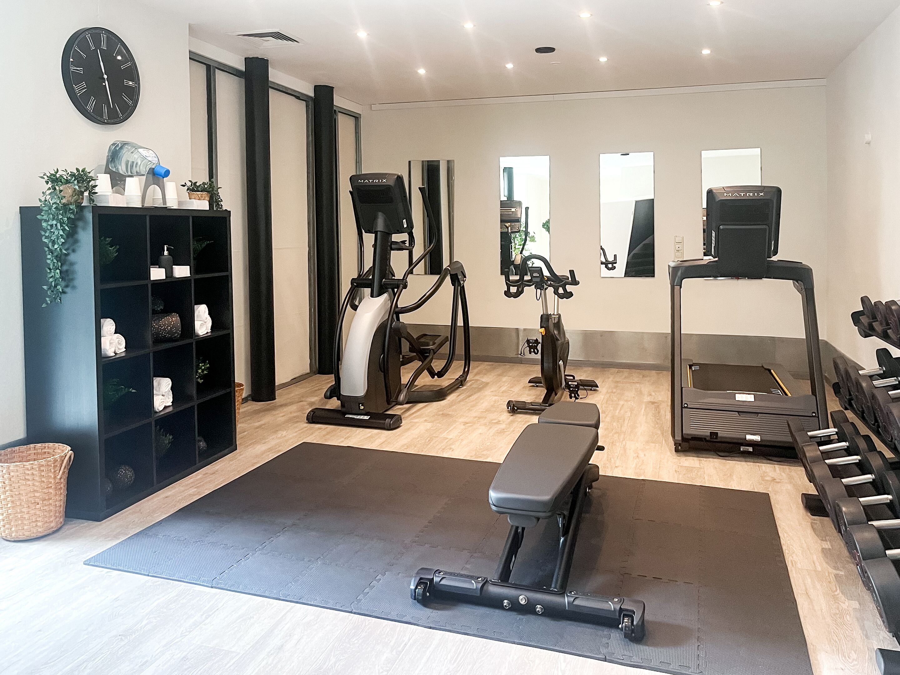 A gym with exercise equipment, a bench, and a mirrored wall.