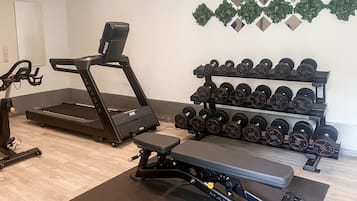 Un gimnasio con cinta de correr, banca para pesas y mancuernas.