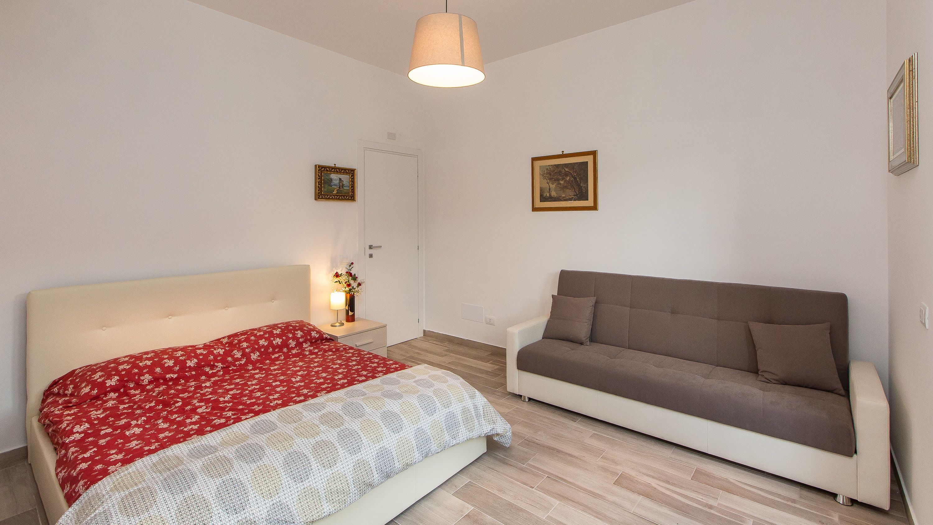 Quarto com cama, sofá, luminária e duas imagens emolduradas na parede.