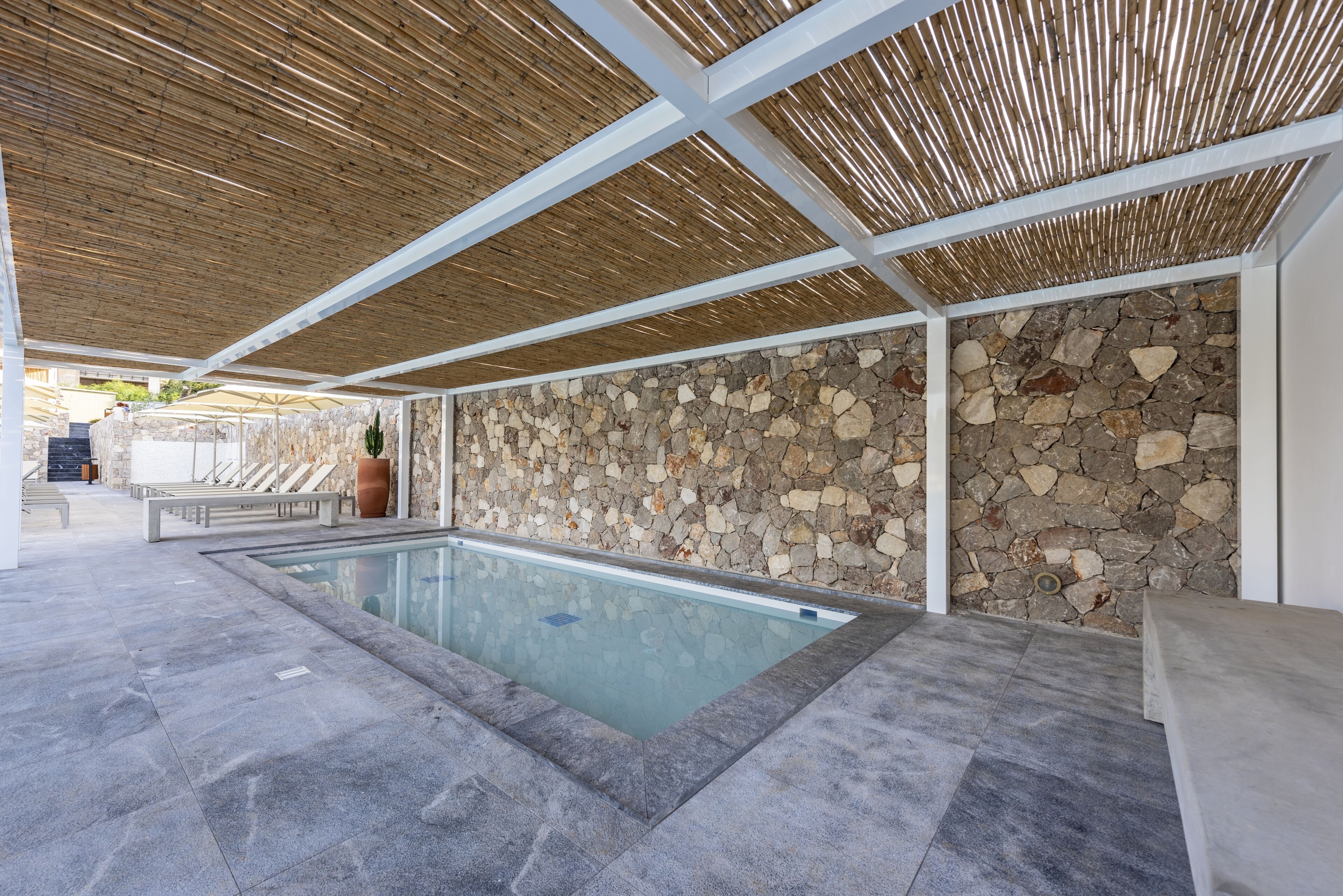 A modern indoor pool area with stone walls and a bamboo ceiling.