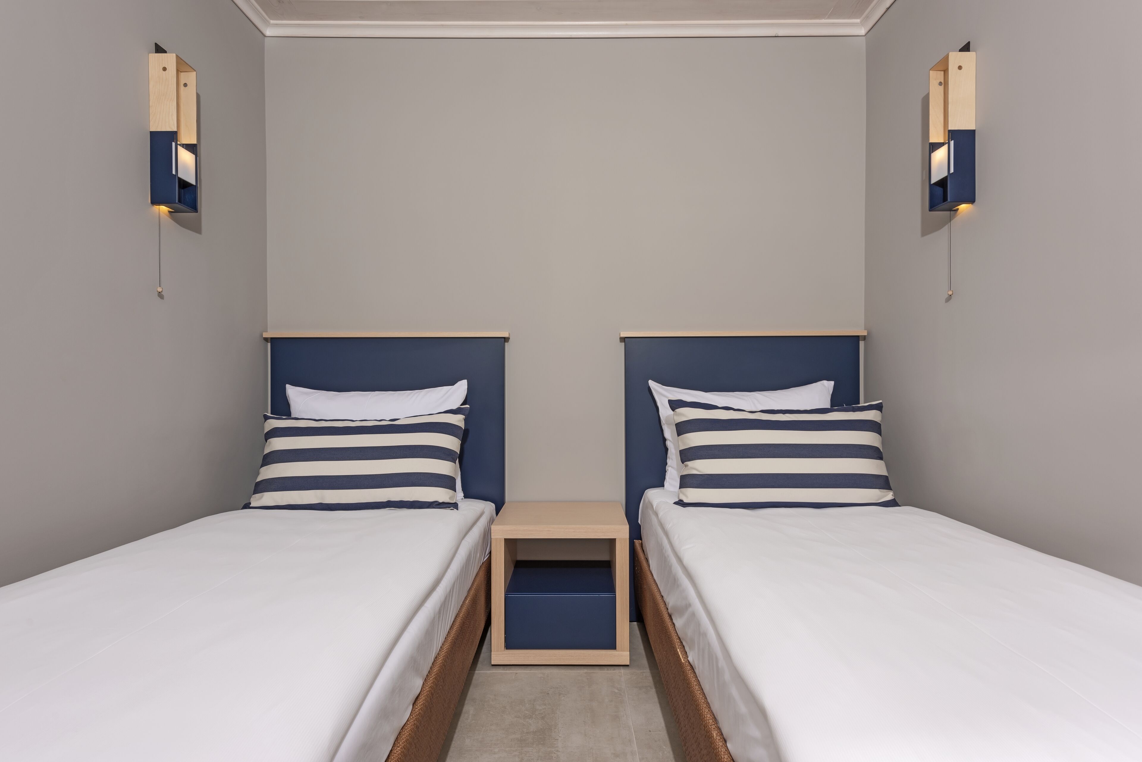 A twin room with two single beds, a small wooden nightstand between them, and wall-mounted light fixtures.
