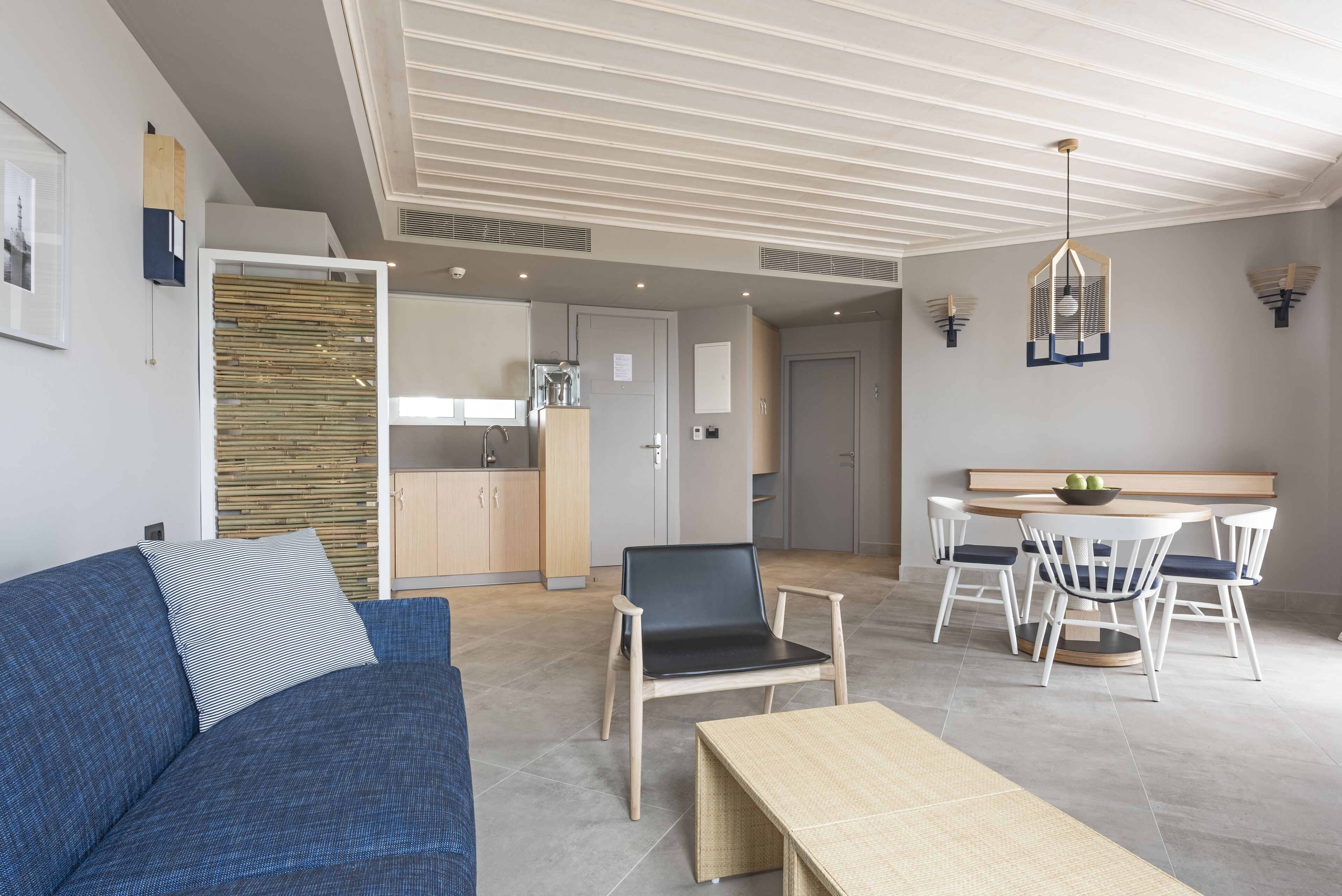 A modern living room with a blue sofa, a wooden coffee table, and a dining area with white chairs and a round table.