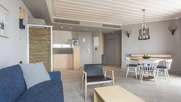 A modern living room with a blue sofa, a wooden coffee table, and a dining area with white chairs and a round table.