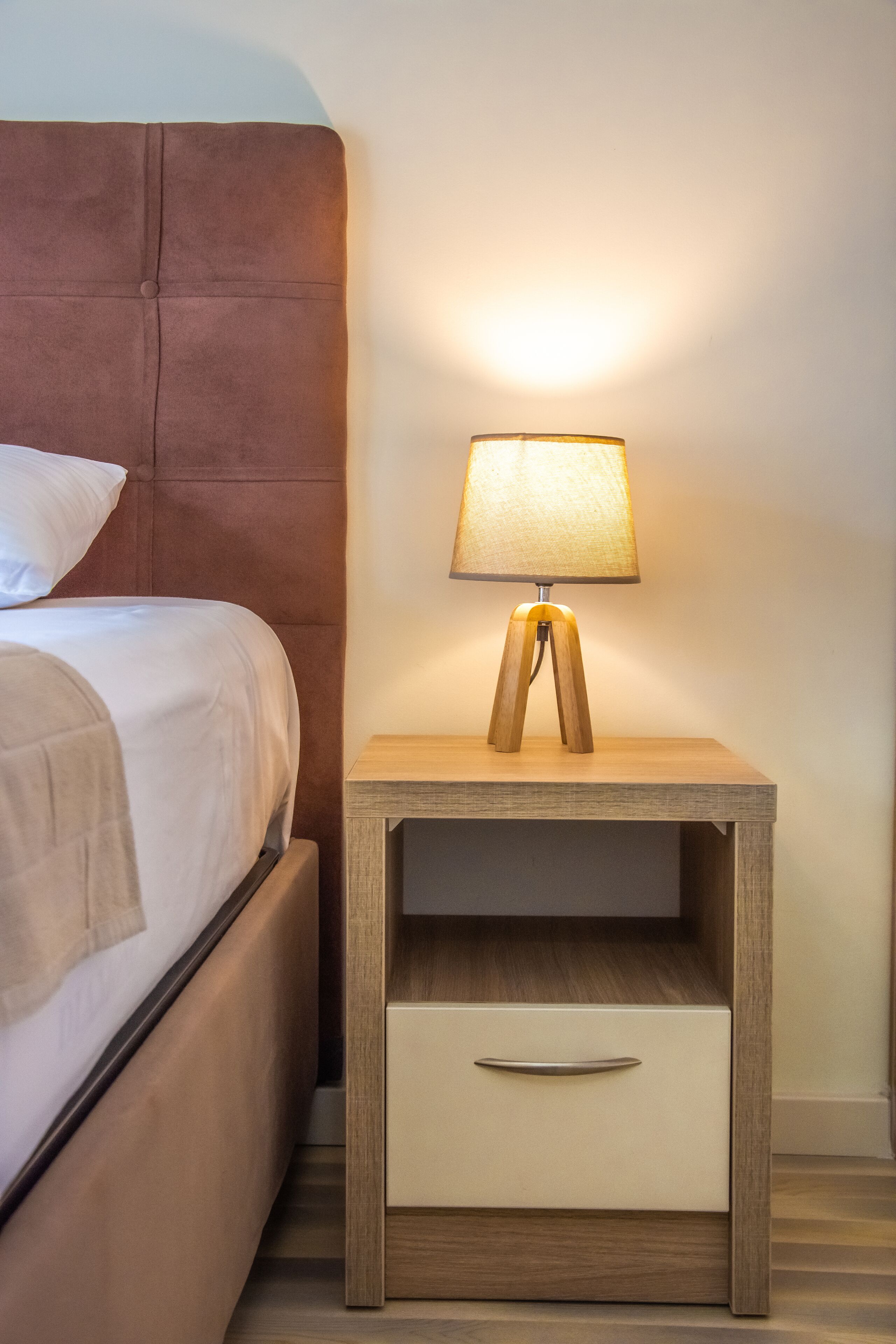 A neatly made bed with a headboard, a bedside table with a lamp, and a drawer.