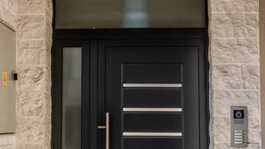 A black door with a vertical glass panel and a horizontal handle, set in a stone wall. - Apartmani Ralux Tivat (Tivat)