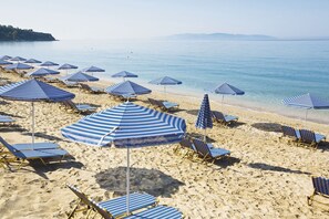 Ein Strand mit blauen, gestreiften Sonnenschirmen und Liegestühlen.