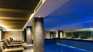 Piscina interior moderna com teto estrelado, espreguiçadeiras e vista para uma floresta através de uma grande janela.