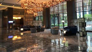 Um hall amplo com um lustre moderno, assentos confortáveis e grandes janelas que oferecem vista para o exterior.