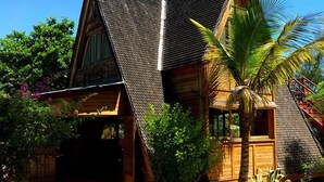 A wooden house with a steeply pitched roof, surrounded by lush greenery and a palm tree. - Bamboo Club (Ifaty)