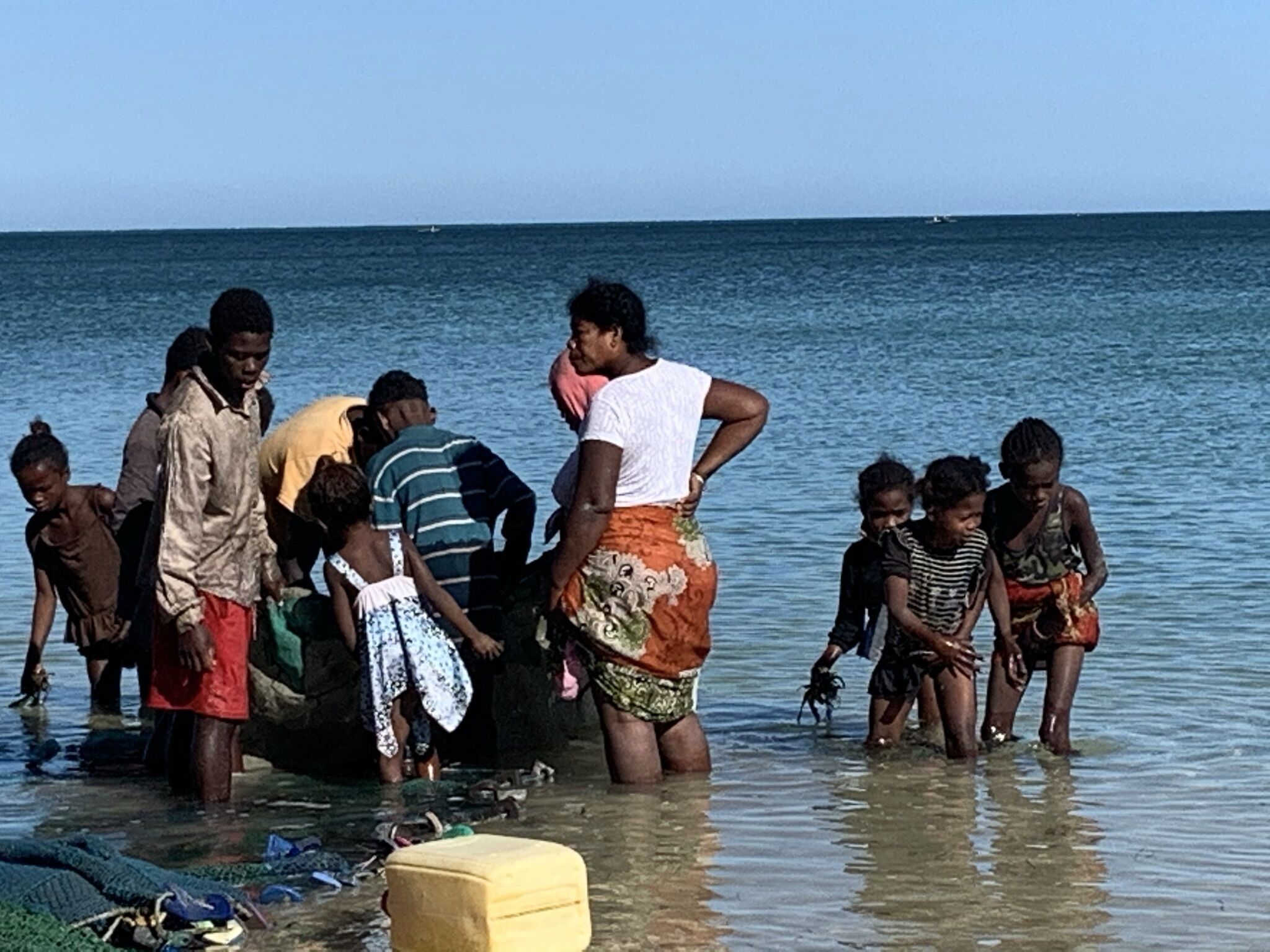 A group of people standing in shallow water, possibly at a beach or riverbank.
