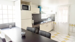 Eine kompakte Küche mit Mikrowelle, Herd und Spüle. Zwei Stühle stehen am Esstisch, ein Fenster sorgt für natürliches Licht.