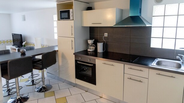Eine moderne Küche mit Mikrowelle, Kaffeemaschine und Backofen. Es gibt einen Essbereich mit Barhocker und Tisch.