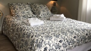 Una cama bien hecha con ropa de cama floral, una lámpara de noche y un cartel motivacional en la pared.