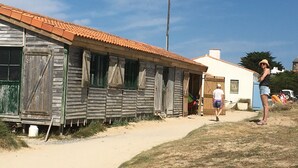 Un edificio rústico de madera con techo de tejas, un sendero de tierra que conduce a él, y un cielo azul despejado.