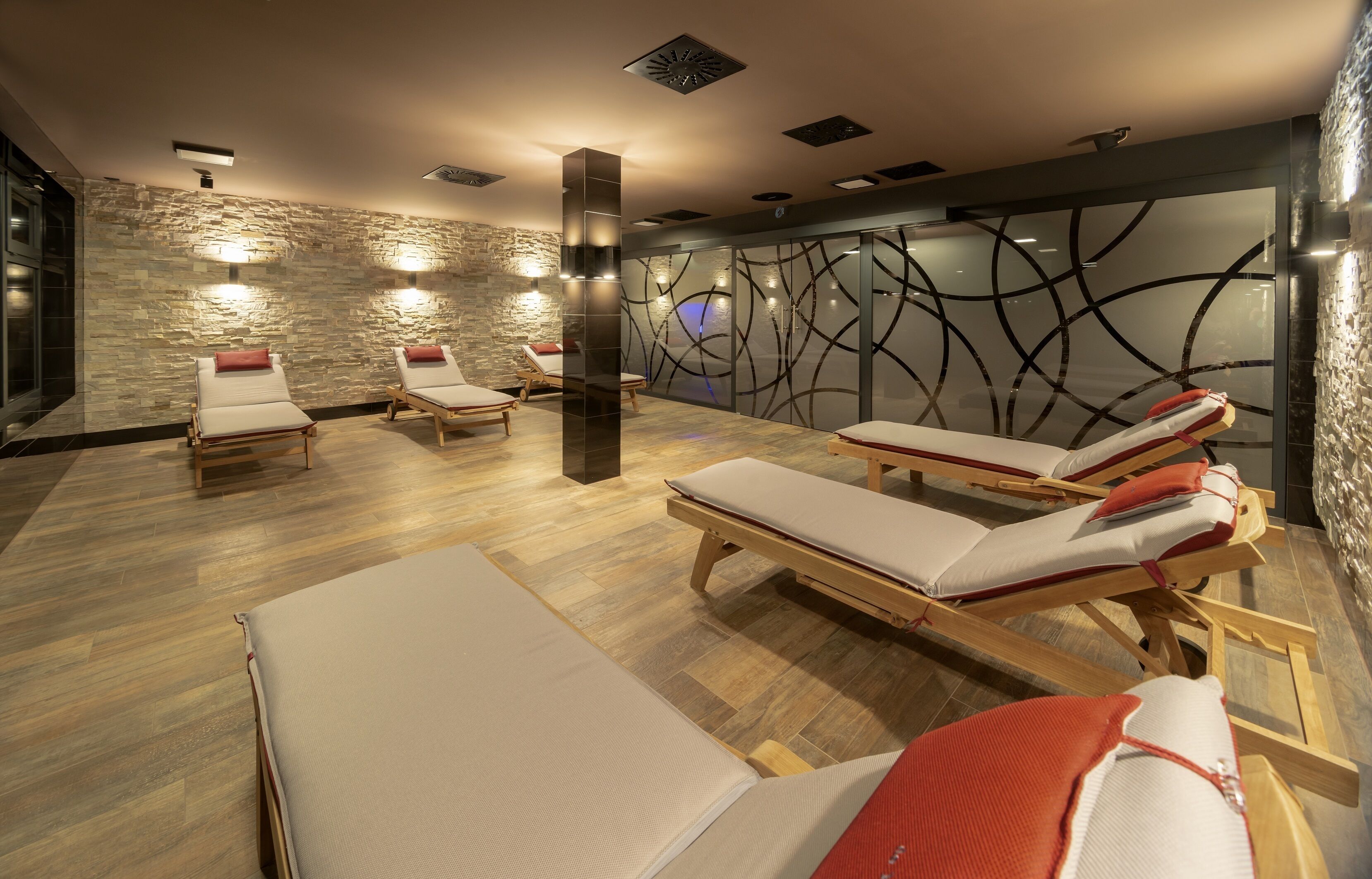 A spa room with wooden floors, stone walls, and sun loungers with red cushions.