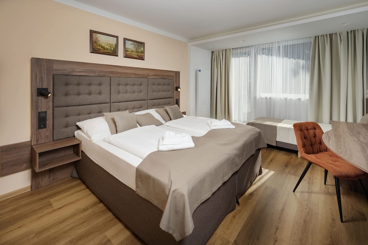 A modern hotel room with a large bed, a bedside table, a chair, and a view of the outdoors through sheer curtains.