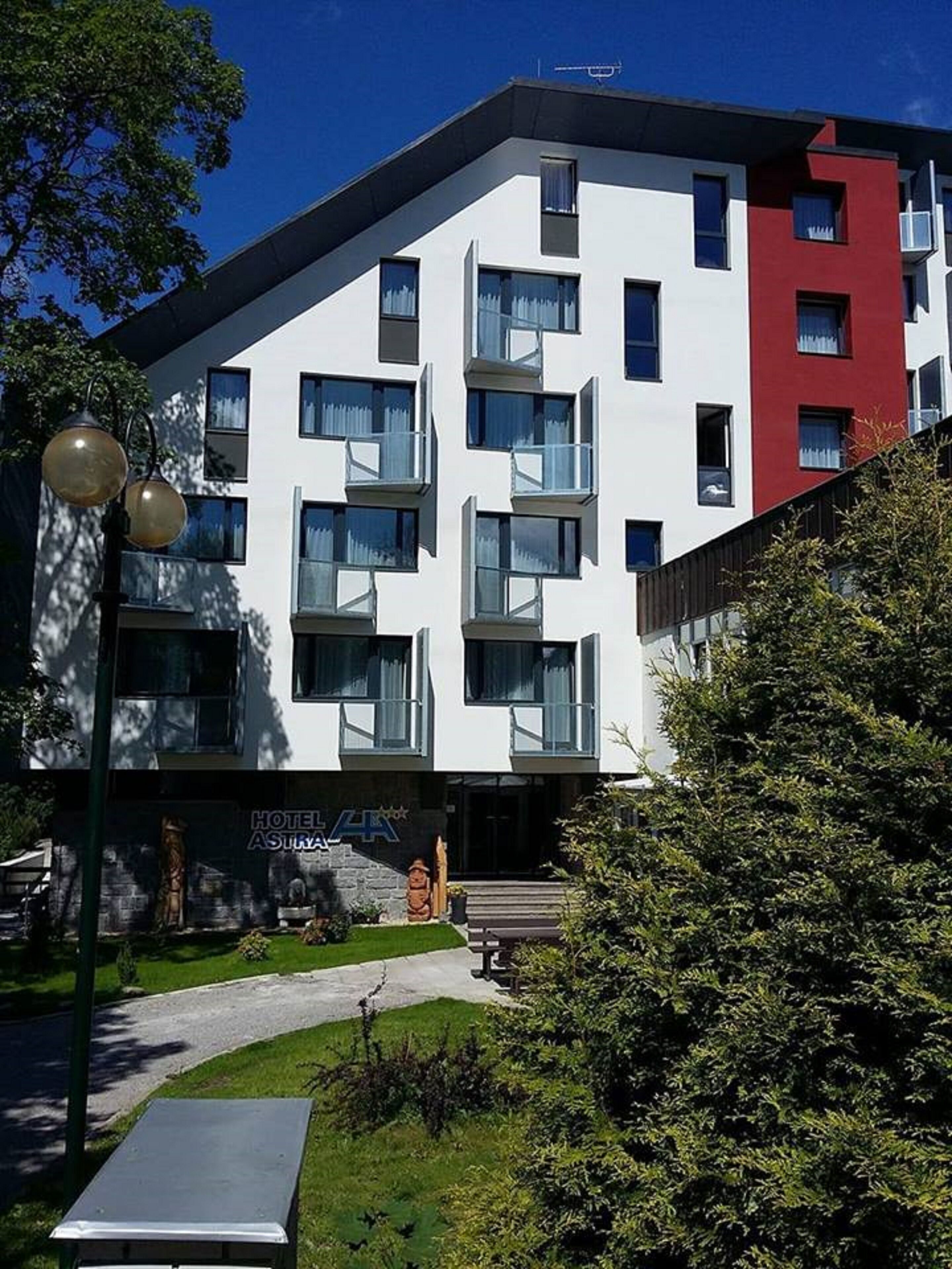 A modern multi-story hotel with a white facade and red accents, featuring balconies and large windows.
